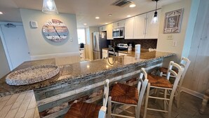 A modern kitchen with a central island, white cabinetry, and a large wall clock.