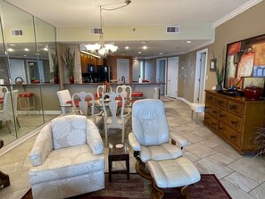 A spacious living room with a dining area, a kitchen in the background, and a large mirror reflecting the space.