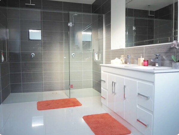 A modern bathroom with a glass shower enclosure, white vanity, and dark tiled walls.