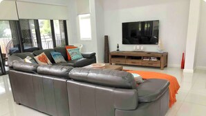A modern living room with a large grey sectional sofa, a wooden TV stand, and a large flat-screen TV mounted on the wall. - Spacious Family Getaway Indoor/Outdoor living close to beach, shops & wineries  (Dromana)