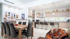 A modern kitchen with a dining area, featuring a wooden table, black chairs, and a tiger-themed chair. - Spacious Family Getaway Indoor/Outdoor living close to beach, shops & wineries  (Dromana)
