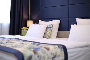 A neatly made bed with white linens and floral-patterned pillows, a dark headboard, and a bedside table with a lamp and a vase of yellow flowers. - Old Town (Sarajevo)