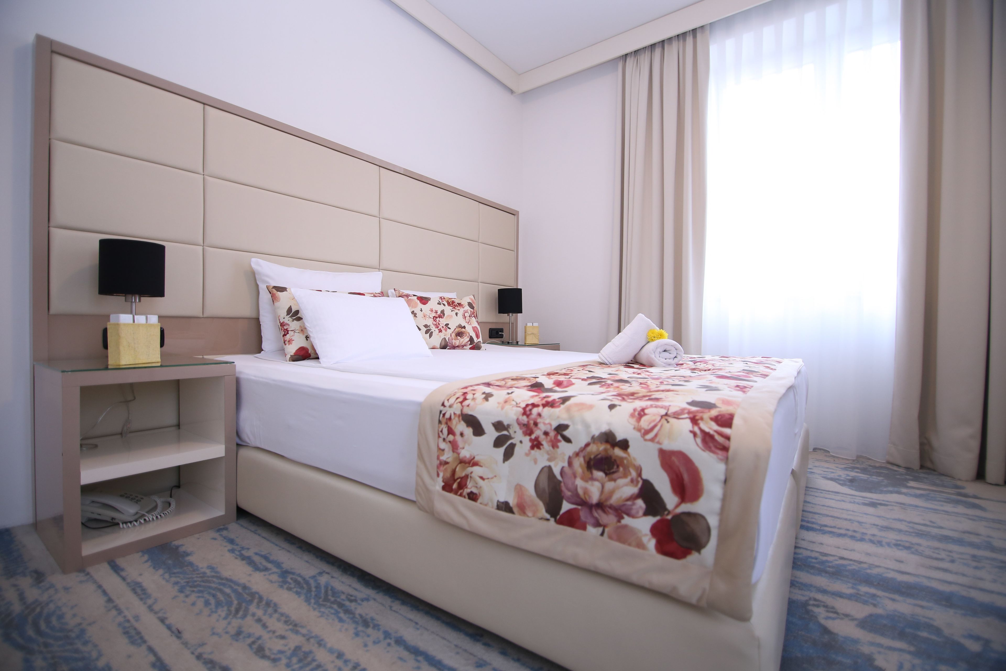 Habitación de hotel con una cama grande, una mesita de noche, una lámpara y una ventana con cortinas.