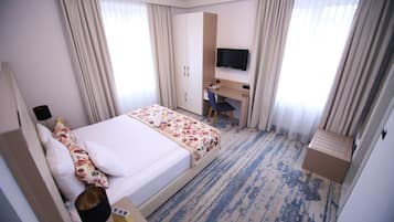 A hotel room with a bed, a desk, a chair, a television, and a wardrobe.