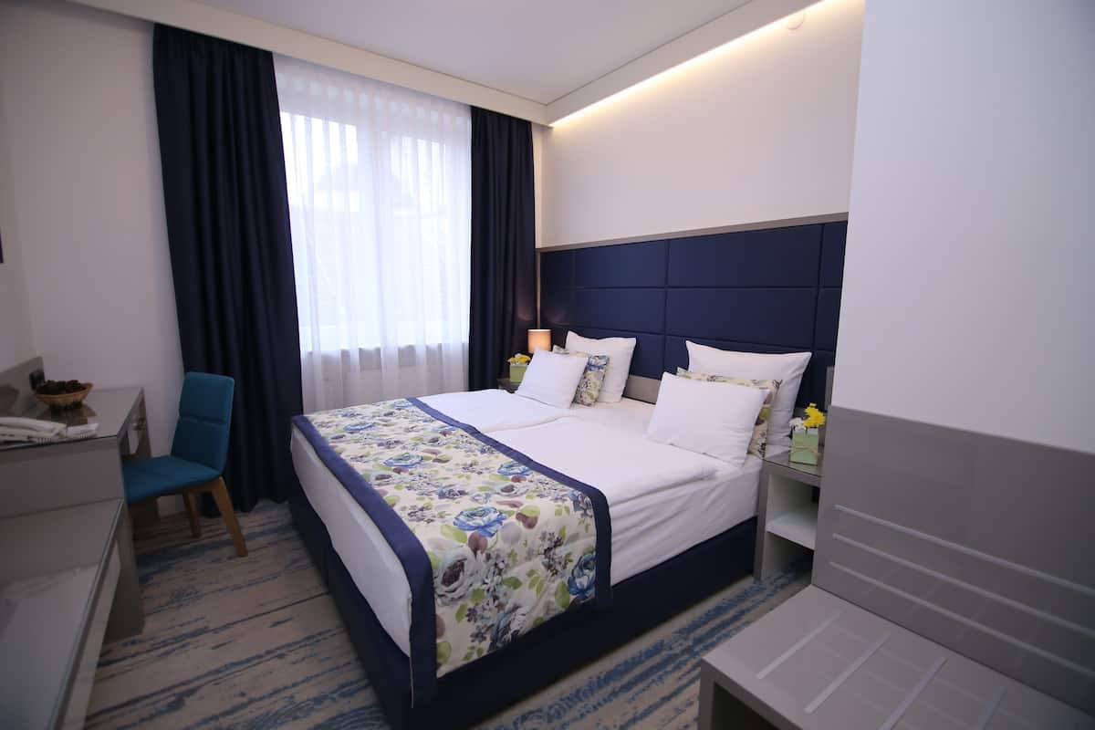 Habitación de hotel con una cama grande, un escritorio, una silla y una mesita de noche con lámpara.