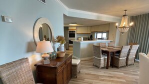 A spacious living area with a dining table, wicker chairs, a wooden cabinet, and a chandelier. - Gulf Front Condo with Stunning Views! (Pensacola)