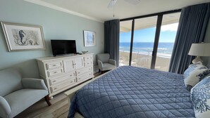 A bedroom with a bed, a TV on a dresser, a chair, and a view of the beach. - Gulf Front Condo with Stunning Views! (Pensacola)