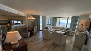A spacious living area with a dining table, sofas, and a large window offering a view of the ocean. - Gulf Front Condo with Stunning Views! (Pensacola)