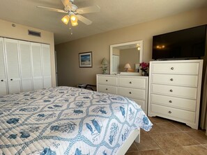 Un dormitorio con cama, cómoda, televisor y ventilador de techo.