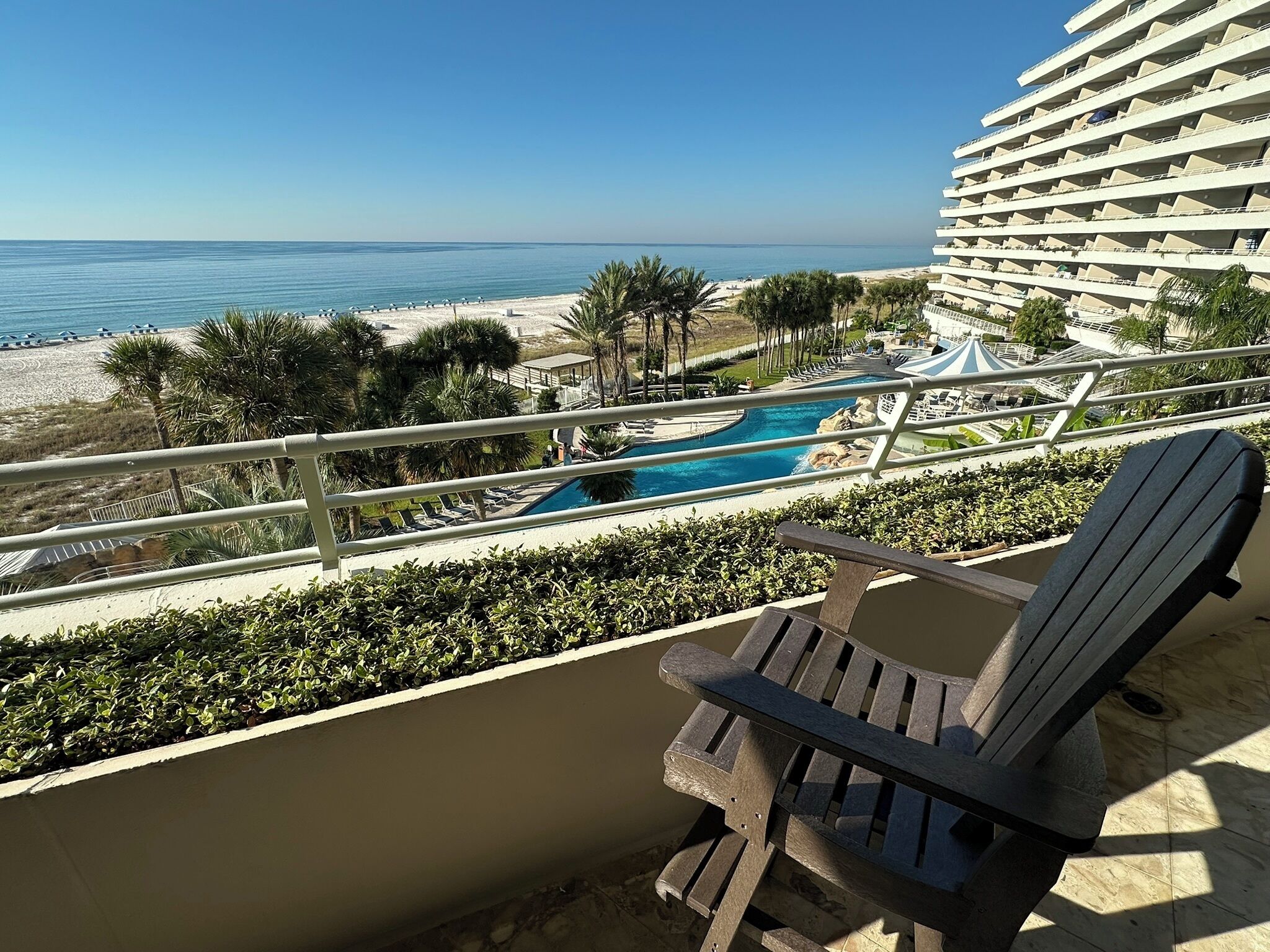 A balcony with a view of a swimming pool and beach, overlooking the ocean.