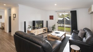 A modern living room with a black leather sofa, a wooden coffee table, and a TV on a wooden stand. - @WineNwaves Margaret River (Margaret River)