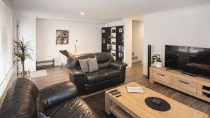 A modern living room with a leather sofa, a wooden coffee table, a TV, and a bookshelf. - @WineNwaves Margaret River (Margaret River)