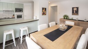 A modern kitchen with white cabinets, a microwave, and an oven. There is a dining table with white chairs and a glass bowl on the table. - @WineNwaves Margaret River (Margaret River)