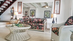 A living room with a sofa, a round wicker table, and a chair. There is a staircase with a wooden railing and a ceiling fan. - Beautiful beachfront at The Villas On Great Bay (Philipsburg)
