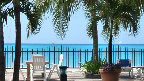 A beachside patio with white chairs, a table, and a large potted plant. - Beautiful beachfront at The Villas On Great Bay (Philipsburg)