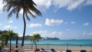 A pool area with lounge chairs, palm trees, and a view of a cruise ship in the distance. - Beautiful beachfront at The Villas On Great Bay (Philipsburg)