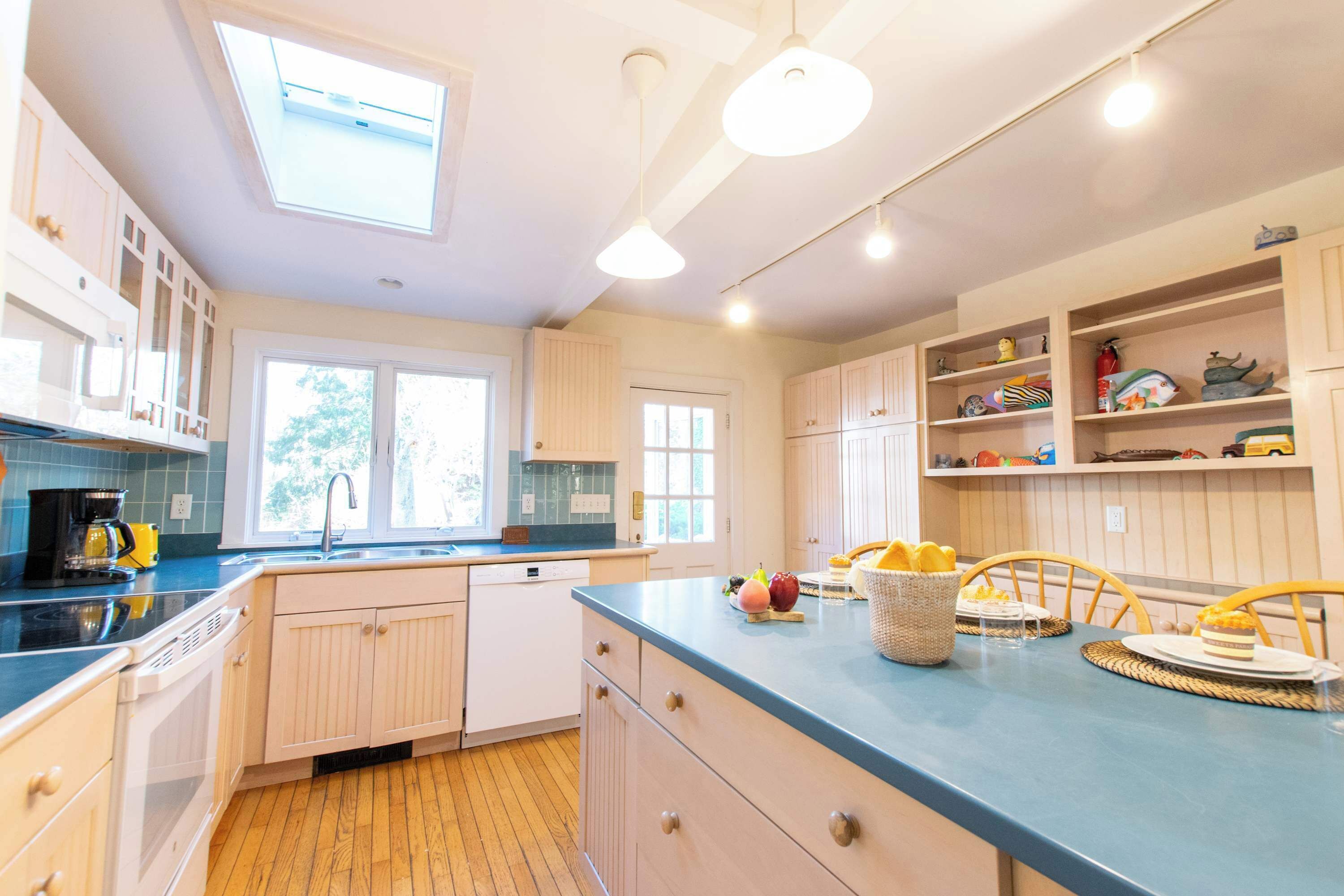 A modern kitchen with white cabinets, a blue countertop, and a skylight.