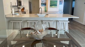 Een moderne keuken met witte kasten, roestvrijstalen apparatuur en een centraal keukenblok met barstoelen.