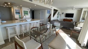 Een moderne keuken met een centraal eiland, barstoelen en een eethoek met een glazen tafel en stoelen.