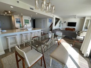 A modern kitchen with a central island, bar stools, and a dining area with a glass table and chairs.