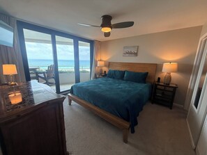 A hotel room with a bed, a desk, a chair, a nightstand, a lamp, and a ceiling fan. - Gulf Front Condo with Stunning Views! (Pensacola)