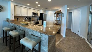 Una cocina moderna con encimeras de granito, electrodomésticos de acero inoxidable y una isla central con taburetes de bar.