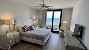 Habitación de hotel con cama, mesitas de noche, escritorio, televisor y vista al océano.