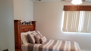A bedroom with a wooden headboard, a bed with striped bedding, a nightstand, a dresser, a ceiling fan, and a window with blinds. - Lake Erie Green Cove Getaway (Oak Harbor)