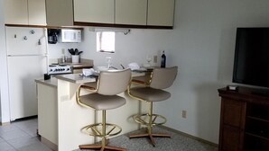 A compact kitchen with a microwave, stove, and two bar stools. - Lake Erie Green Cove Getaway (Oak Harbor)