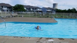 A swimming pool with a person in the water, surrounded by a fence and houses in the background. - Lake Erie Green Cove Getaway (Oak Harbor)
