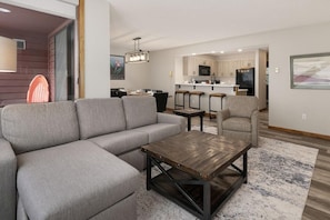 Un salon moderne avec un canapé d’angle, une table basse et un coin cuisine à l’arrière-plan.