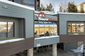 Un bâtiment orné d’une enseigne « Snowblaze », d’un panneau d’avertissement indiquant un risque de chute de glace, et offrant une vue sur un paysage enneigé à travers de grandes fenêtres.
