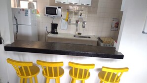 Eine Küche mit schwarzer Arbeitsplatte, weißen Schränken, einer Mikrowelle, einer Kaffeemaschine und drei gelben Stühlen.