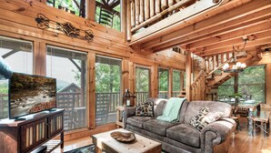 Ein großzügiges Wohnzimmer mit Holzboden, großen Fenstern, einer Couch, einem Couchtisch und einer Treppe.