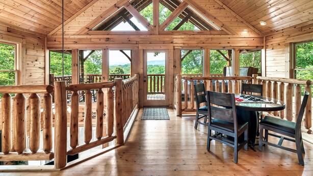 Eine Holzhütte mit hohen Decken, großen Fenstern und einer Terrassenfläche mit Stühlen und Tisch.