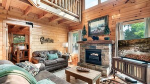 Ein gemütliches Blockhaus-Interieur mit Kamin, einer Couch, einem Couchtisch und einem Fernseher.