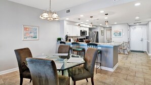 Una cocina moderna con armarios blancos, una isla central y un comedor con mesa y sillas de vidrio.