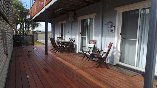 A covered patio with wooden flooring, a table with chairs, and a sliding glass door.