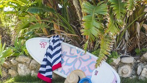 A surfboard with a colorful design, a striped towel, and a straw hat on the grass.