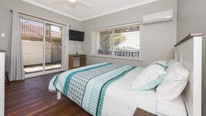 A bedroom with a bed, a ceiling fan, a TV, and a window with blinds.