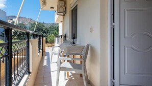 En balkon med bord og stole, en hvid dør, og udsigt over det omkringliggende område.