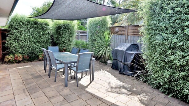 Eine Terrasse mit Tisch, Stühlen, einem Grill und einem großen Sonnensegel.