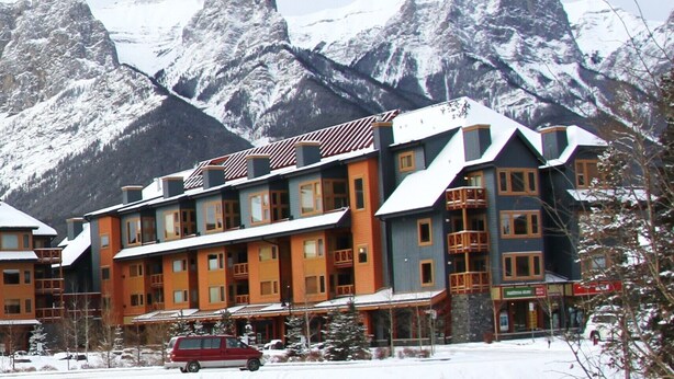 Un hôtel à plusieurs étages, avec une façade évoquant un chalet de ski, de grandes fenêtres et un paysage montagneux en arrière-plan.