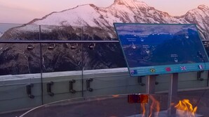 Un foyer avec des flammes, un panneau indicateur avec une carte, et des montagnes enneigées en arrière-plan.