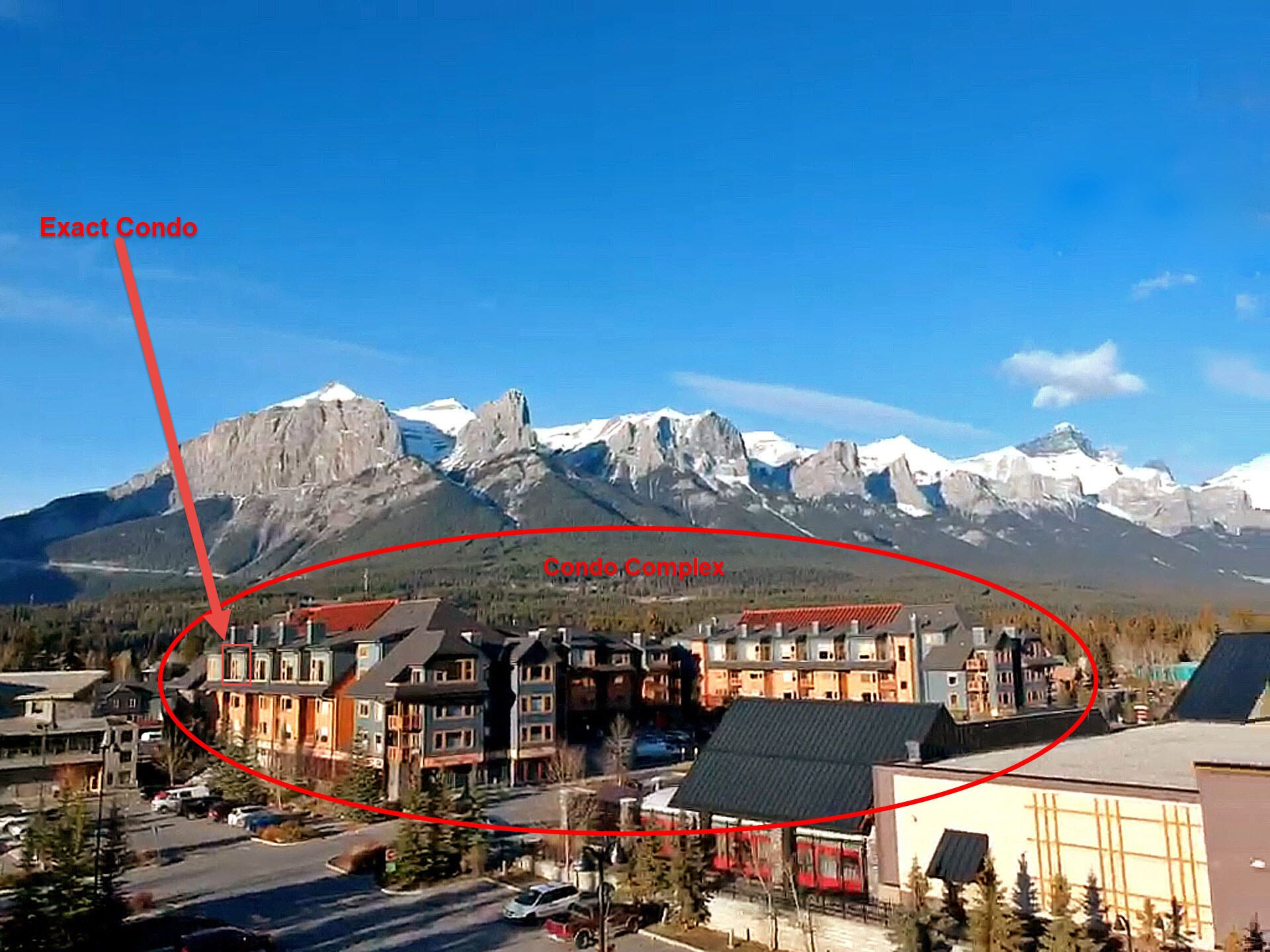 Un complejo de condominios con varios edificios, una calle y montañas al fondo.