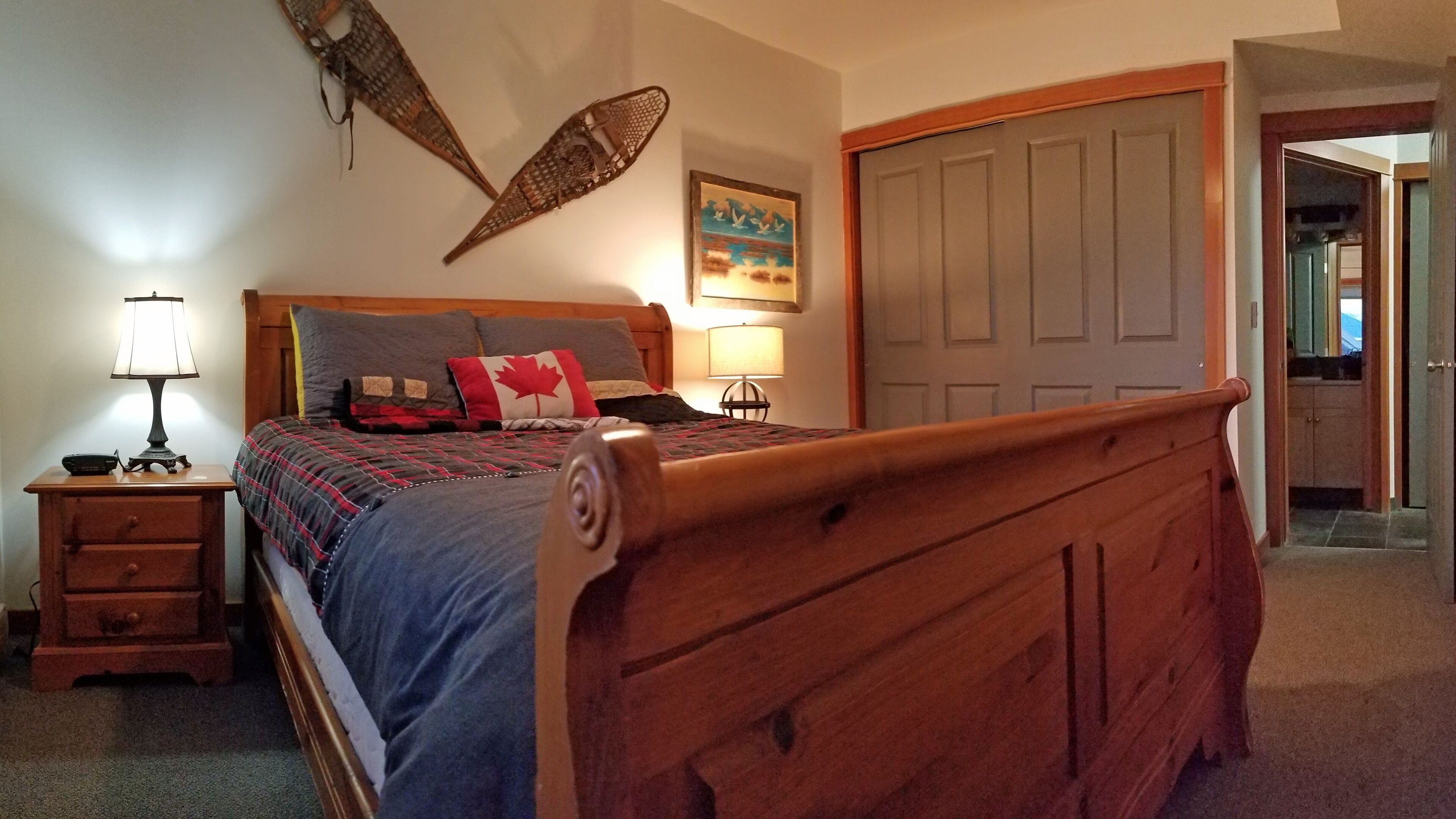 Une chambre à coucher avec un lit en bois, une table de chevet avec une lampe, une commode, une décoration murale et une porte.