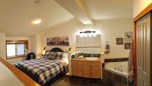 Une chambre à coucher comprenant un lit, une table de chevet, une commode, une fenêtre et une salle de bain avec un lavabo, un miroir et une baignoire.