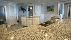 A kitchen with granite countertops, white cabinetry, and a stainless steel sink. - Gulf Front Condo with Stunning Views! (Pensacola)