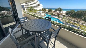 A balcony with a round table and chairs, overlooking a swimming pool and a hotel building. - Gulf Front Condo with Stunning Views! (Pensacola)