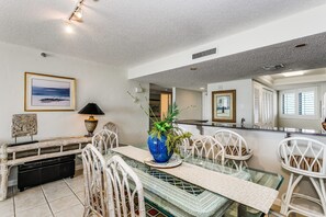 A dining area with a glass table, white chairs, a blue vase with plants, and a framed picture on the wall. - Gulf Front Condo with Stunning Views! (Pensacola)